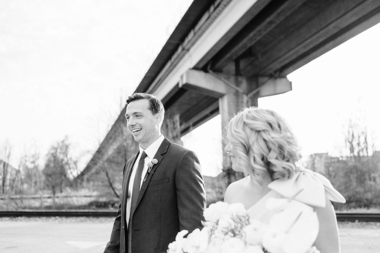 A romantic black and white wedding photo with a couple looking at each other by a bridge.