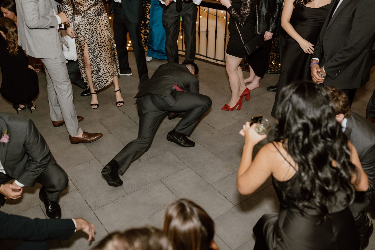 Wedding guests dancing enthusiastically on a tiled floor at the reception.