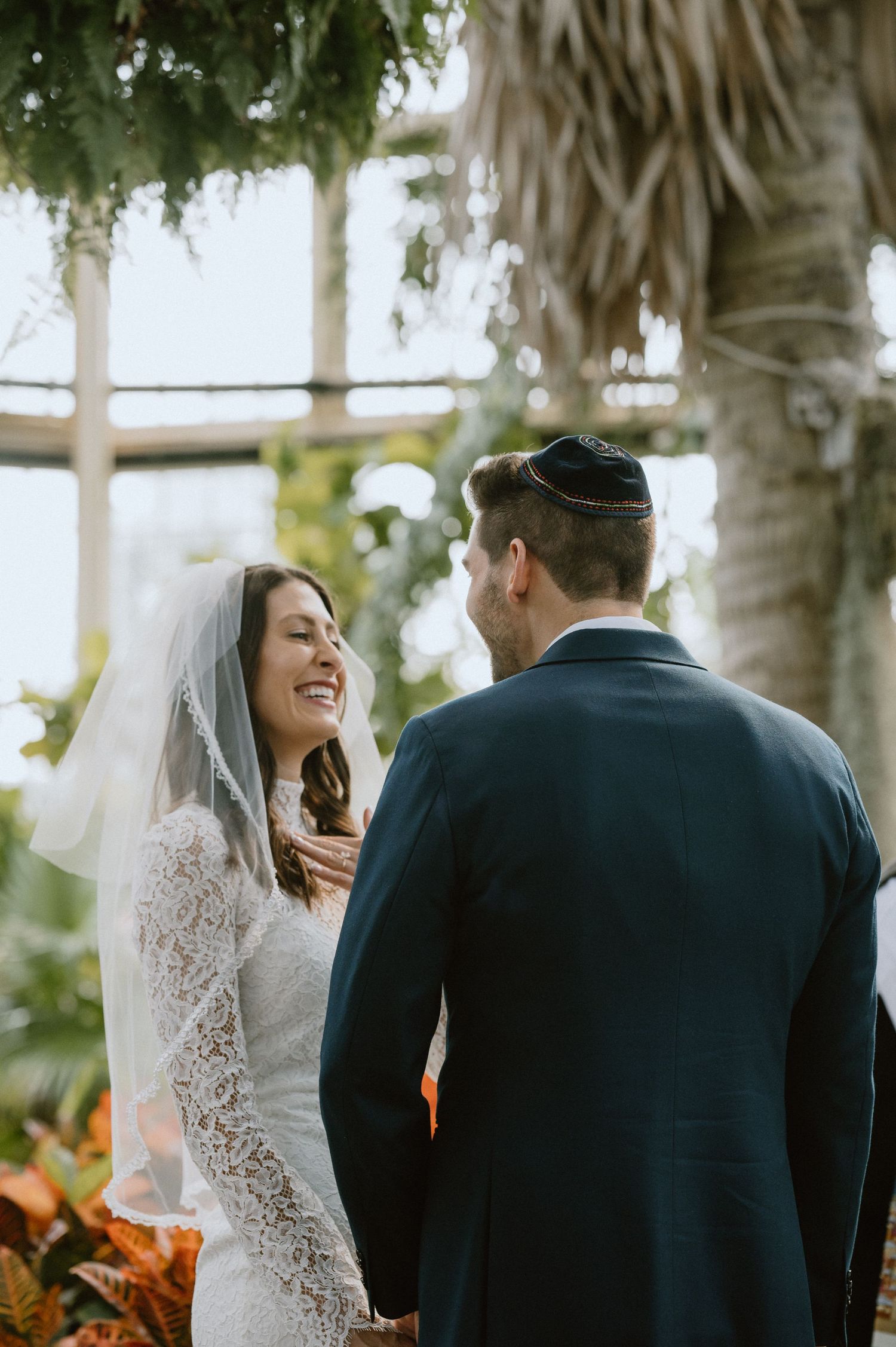 A couple shares an intimate moment during their wedding ceremony in a sunlit conservatory.