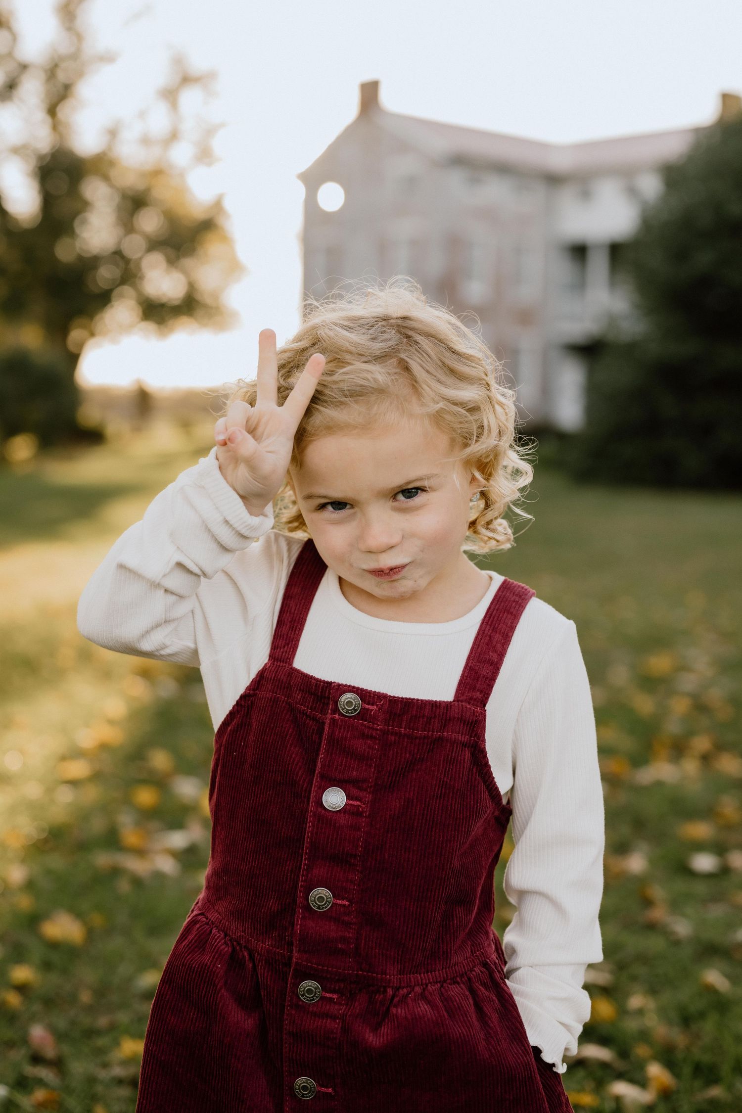Child in burgundy corduroy overalls poses in front of historic building during golden hour.