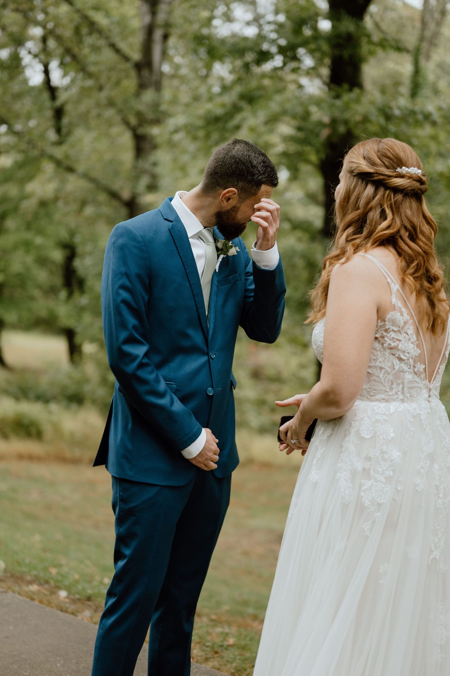 An emotional first look moment between newlyweds in a garden setting with the groom in navy suit wiping tears.
