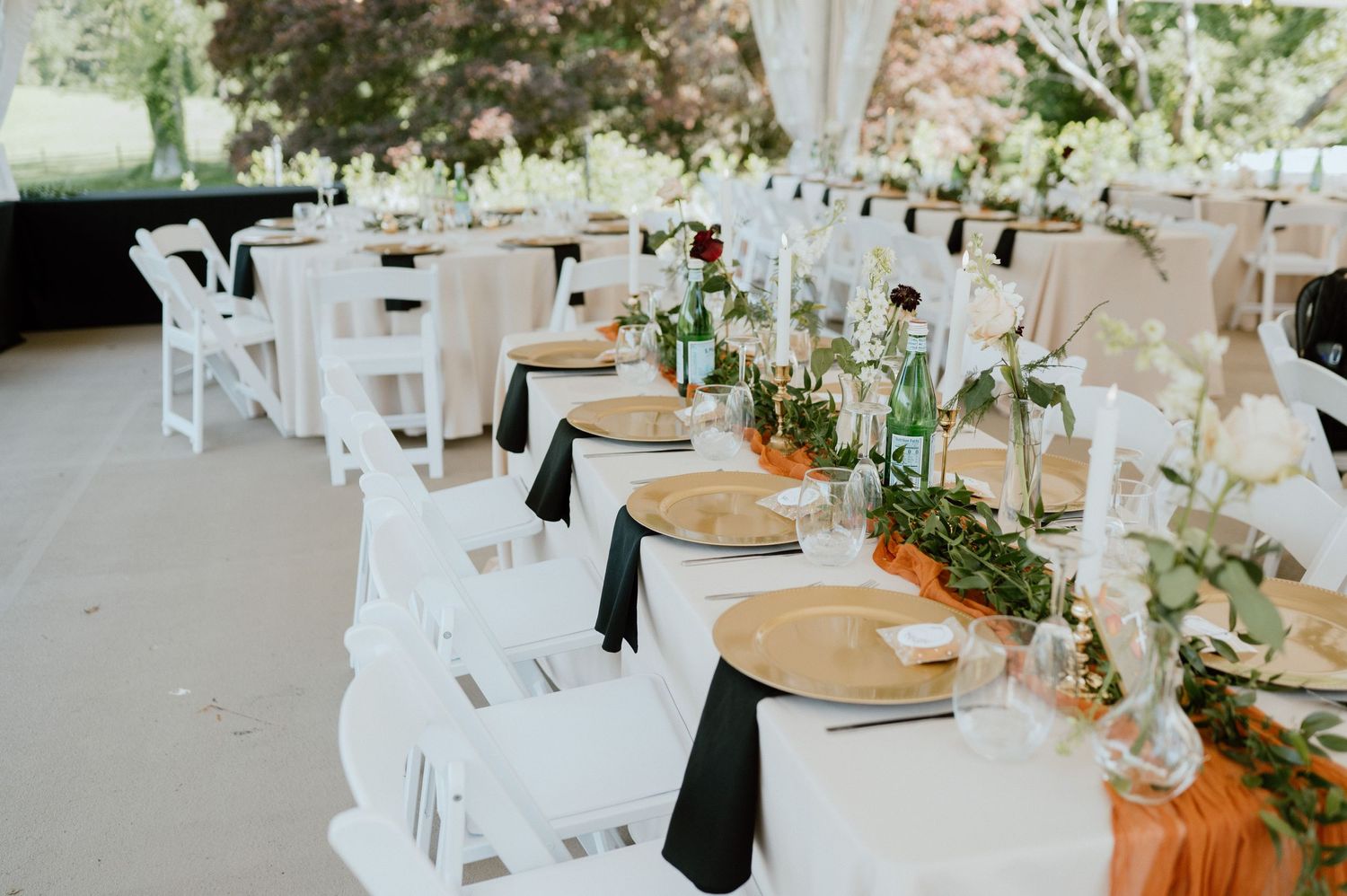 Elegant wedding reception table setup with white linens, rustic place settings and greenery garland centerpieces.