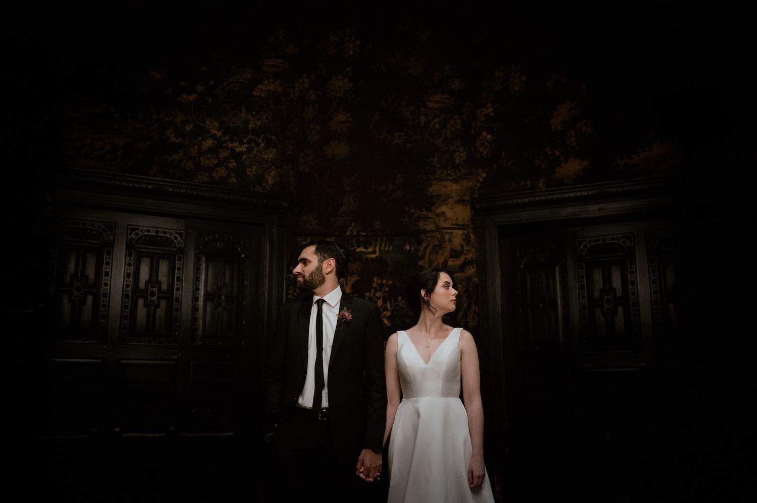 Dramatic wedding portrait in dark vintage room with ornate walls.