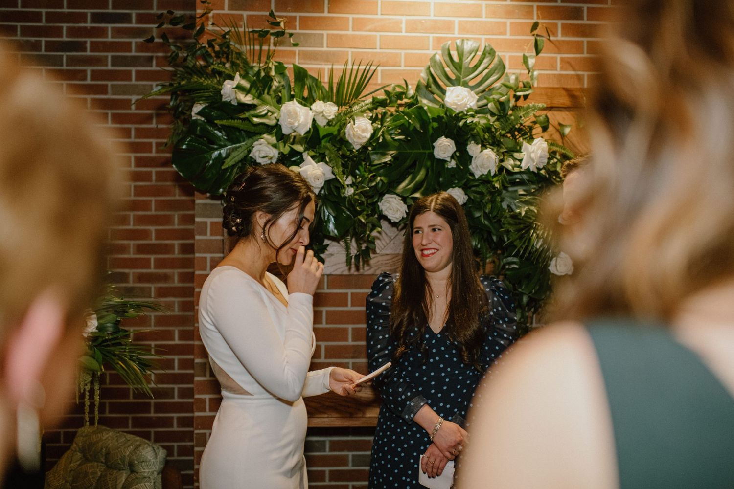 A joyful celebration moment under a lush floral arch against exposed brick walls.