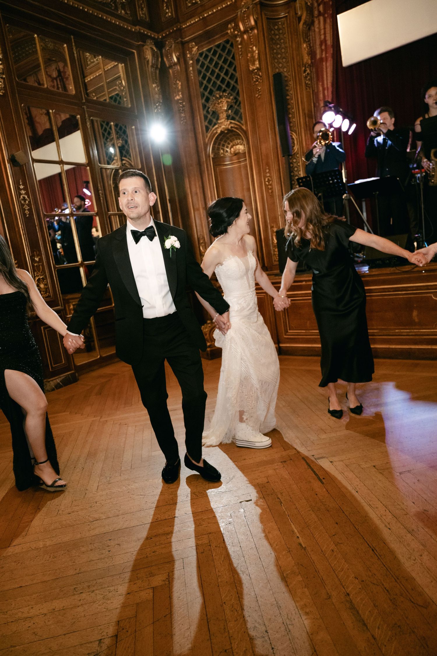 Wedding guests dancing and twirling together on an elegant hardwood dance floor in a grand ballroom.