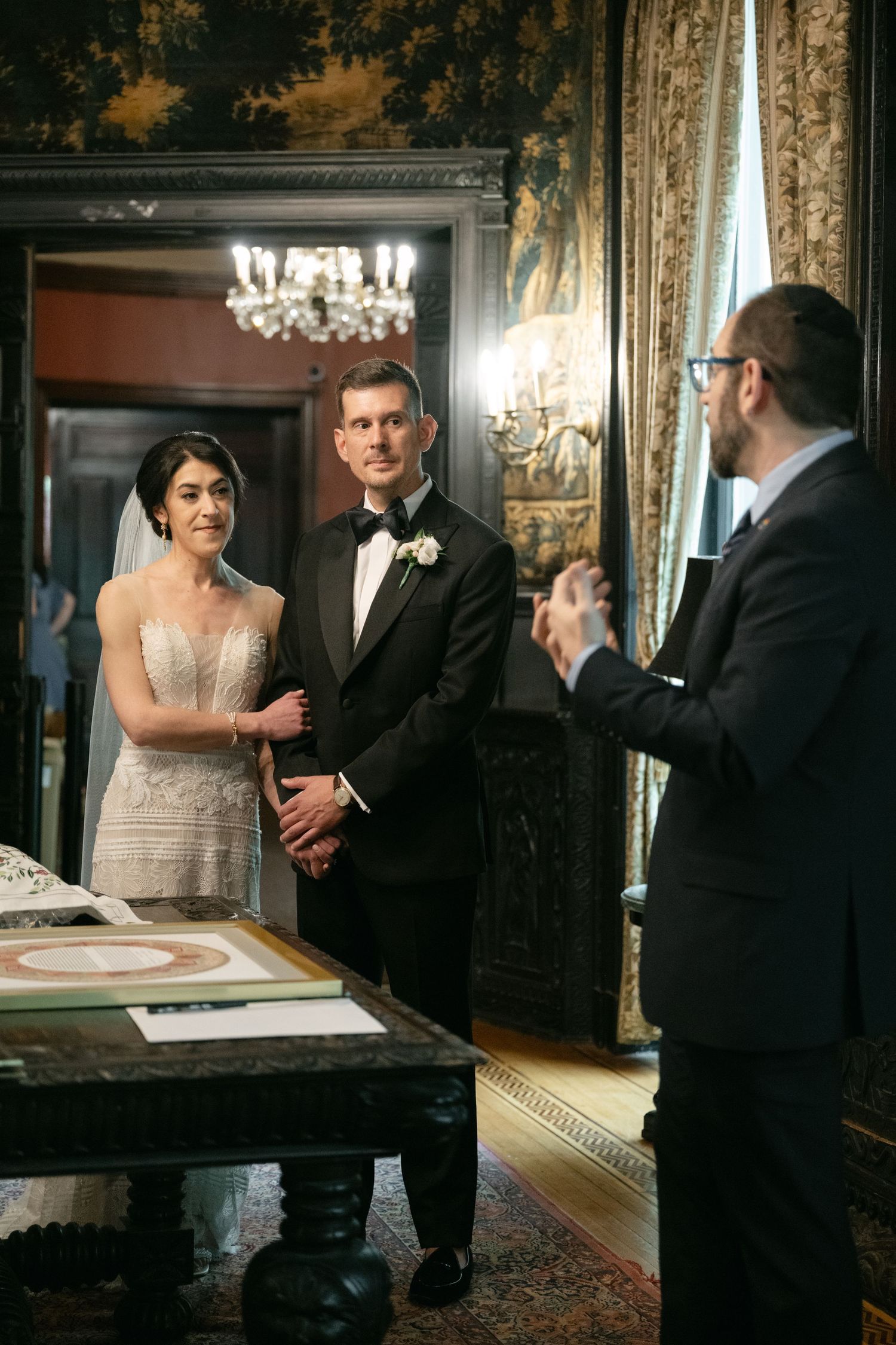 Elegant guests signing a guestbook at a formal wedding ceremony in an ornate room with chandeliers.