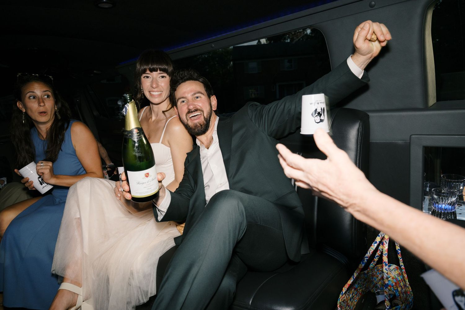 Wedding celebration continues in the back of a limousine with drinks and laughter.