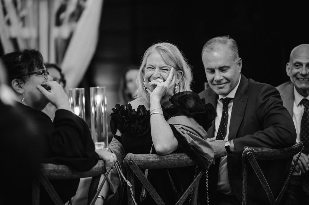 Black and white photo of wedding guests laughing during reception dinner.