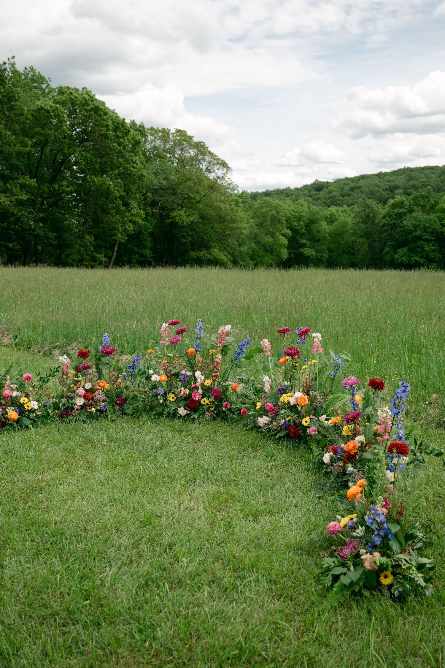 Colorful floral arrangements create a winding path through a lush green meadow under cloudy skies.