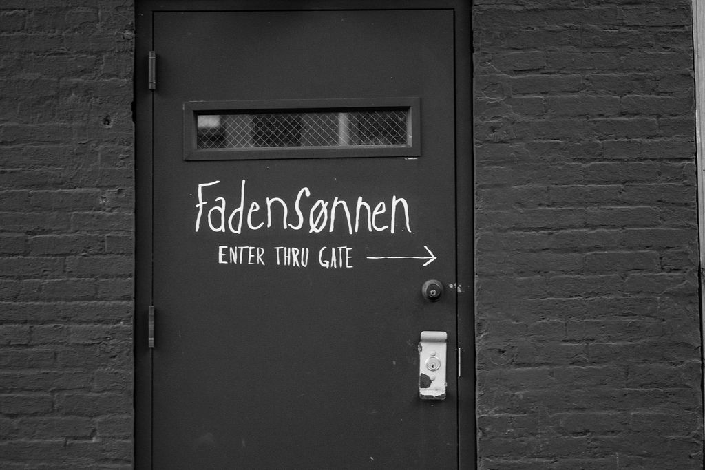 Black painted brick wall with dark doors and minimal text signage.