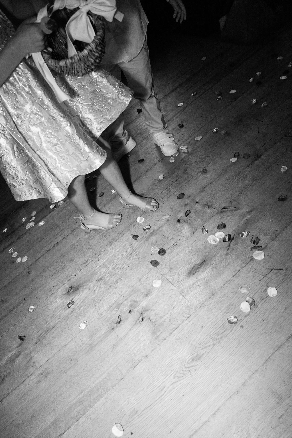 Black and white detail shot of feet and dress hems on a wooden dance floor.