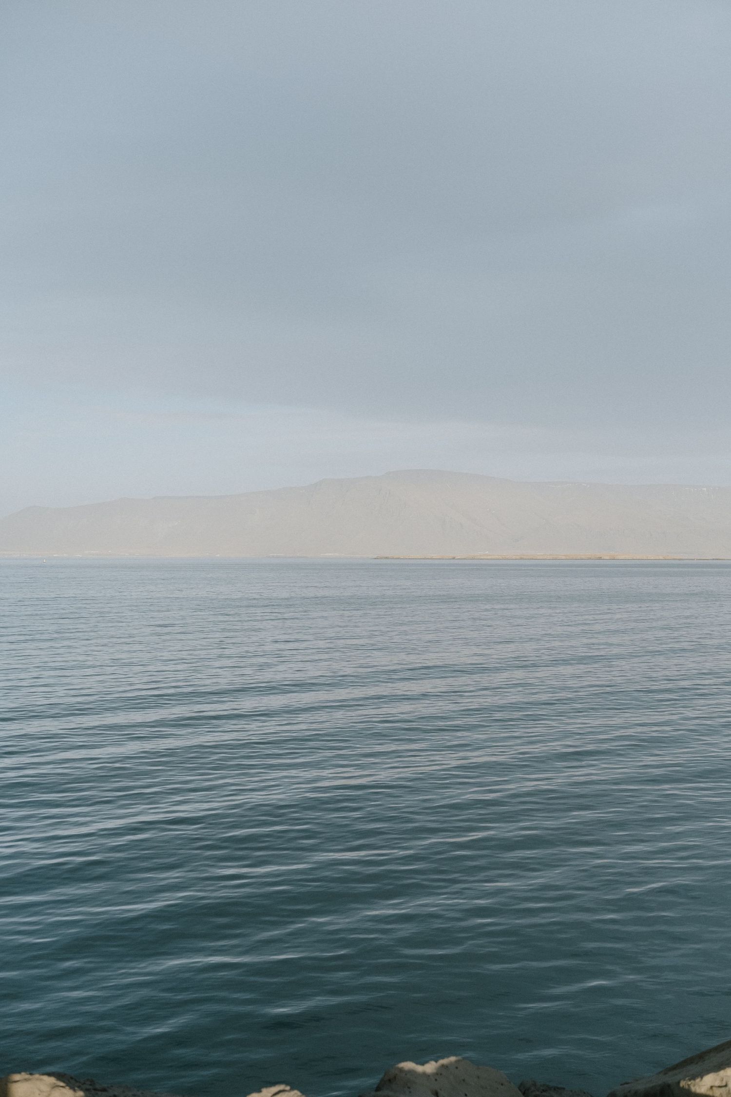 Serene seascape with misty mountains visible across calm waters under an overcast sky.