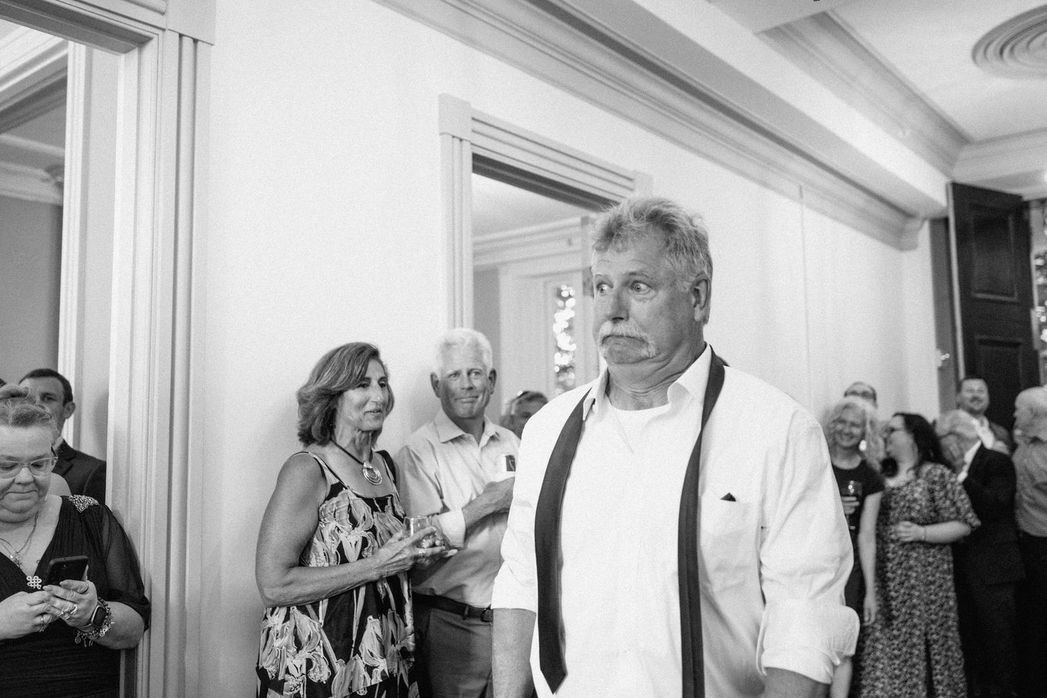 Black and white candid photo of wedding guests mingling at indoor reception.