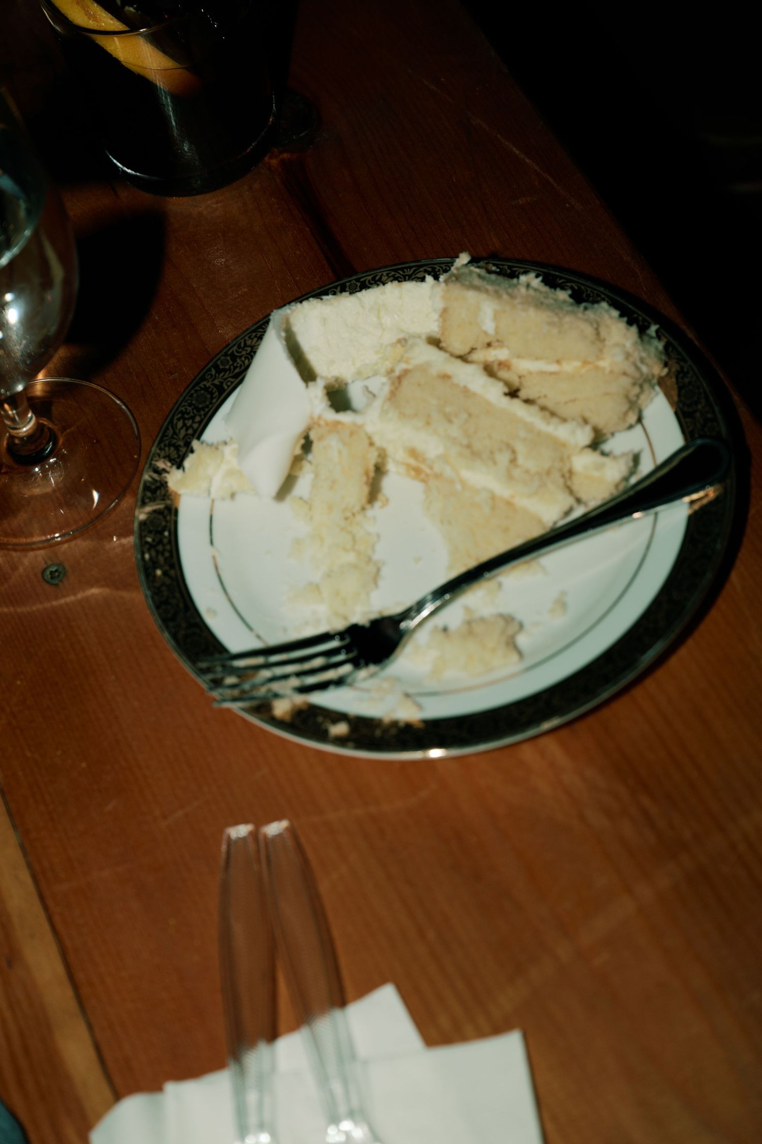 A partially eaten slice of wedding cake on a dark plate with fork and napkin.