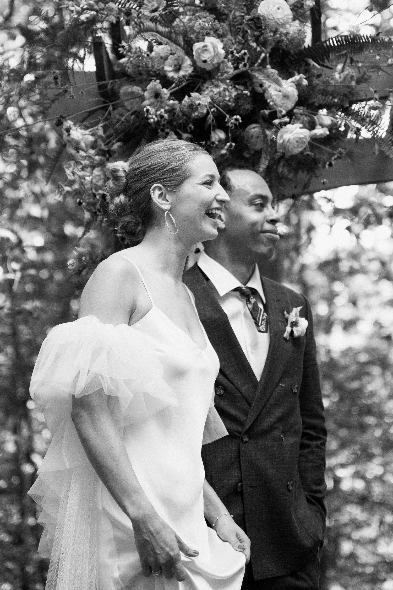 A couple stands together under a floral arch during their outdoor wedding ceremony.