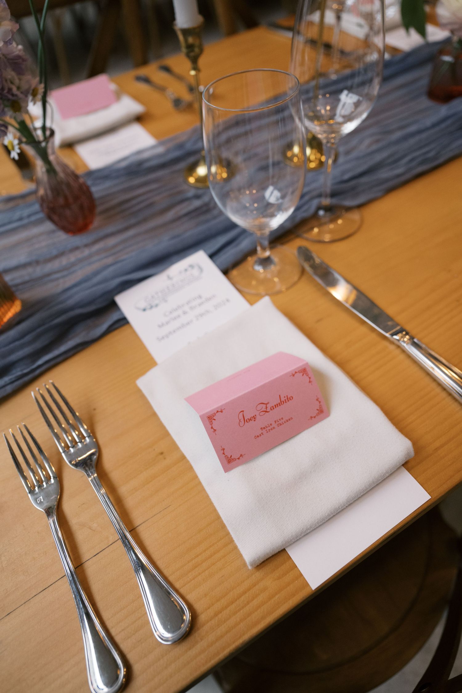 Wedding place setting with white napkin, pink name card, and elegant silverware.