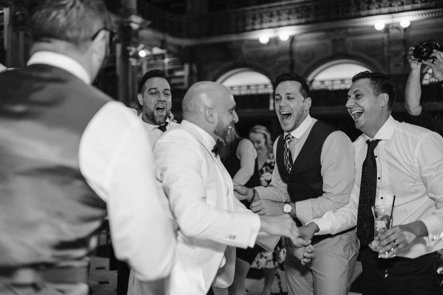 Black and white photo of guests celebrating and dancing at an elegant indoor reception.