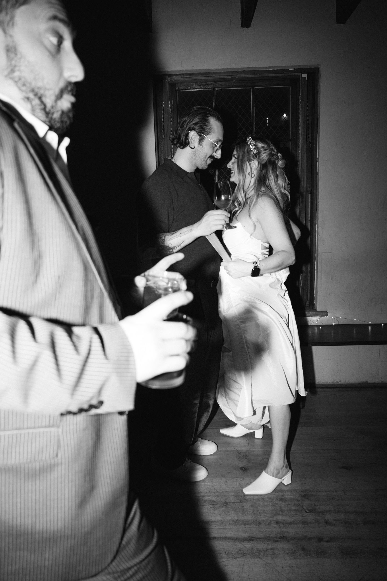 A black and white candid photo captures dancing and celebration at an indoor party.