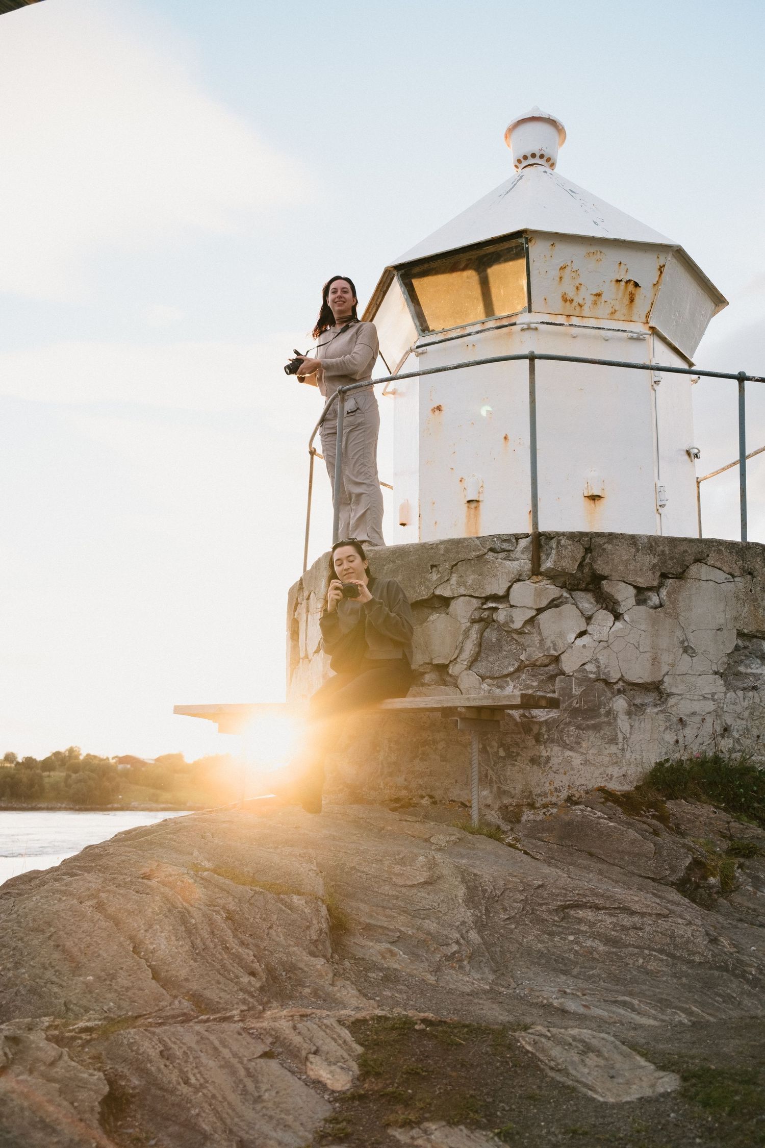 Historic white lighthouse with figure standing at top during golden sunset.