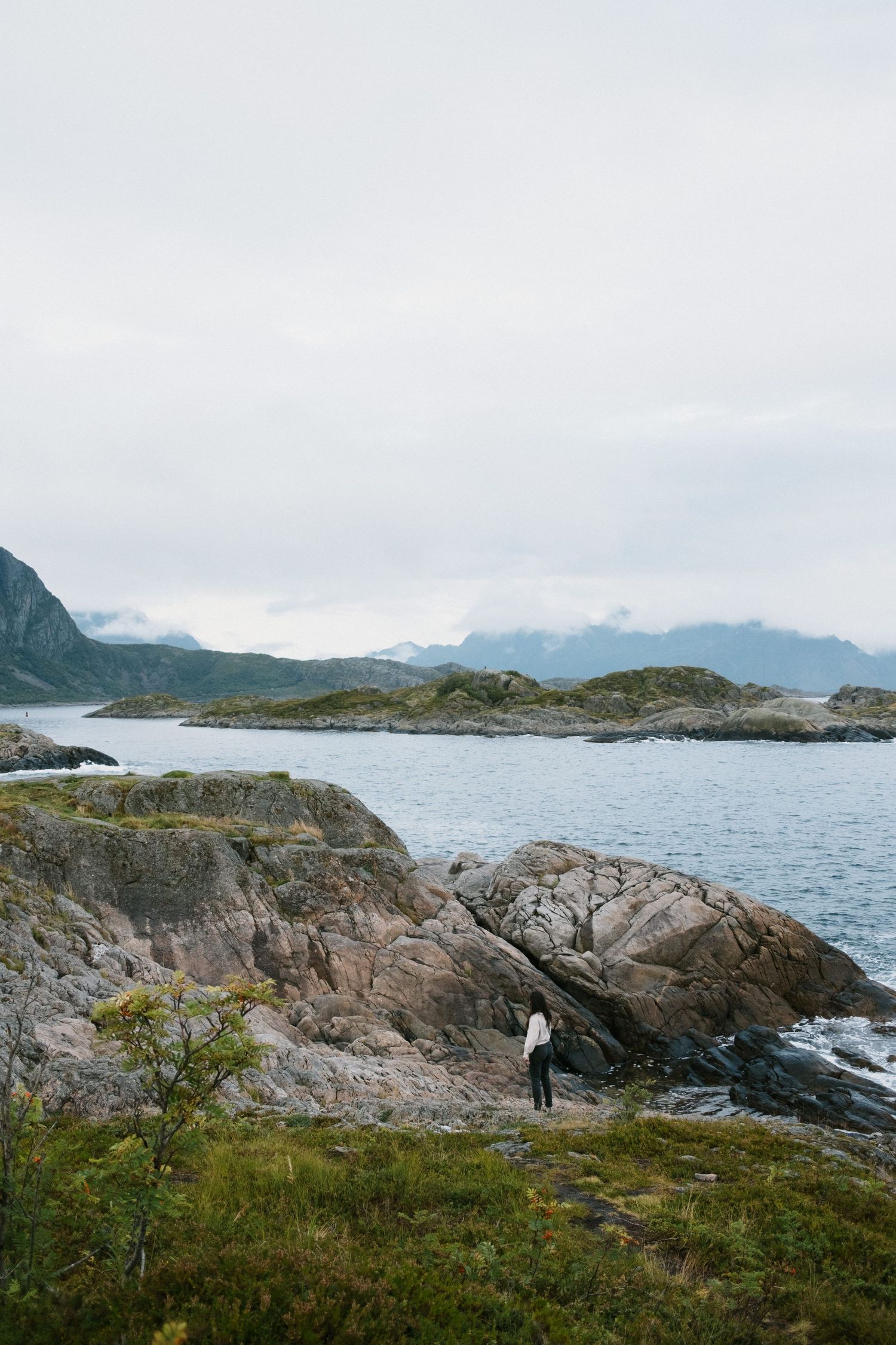 Rocky coastal outcrop with distant mountains and figure standing on the edge.