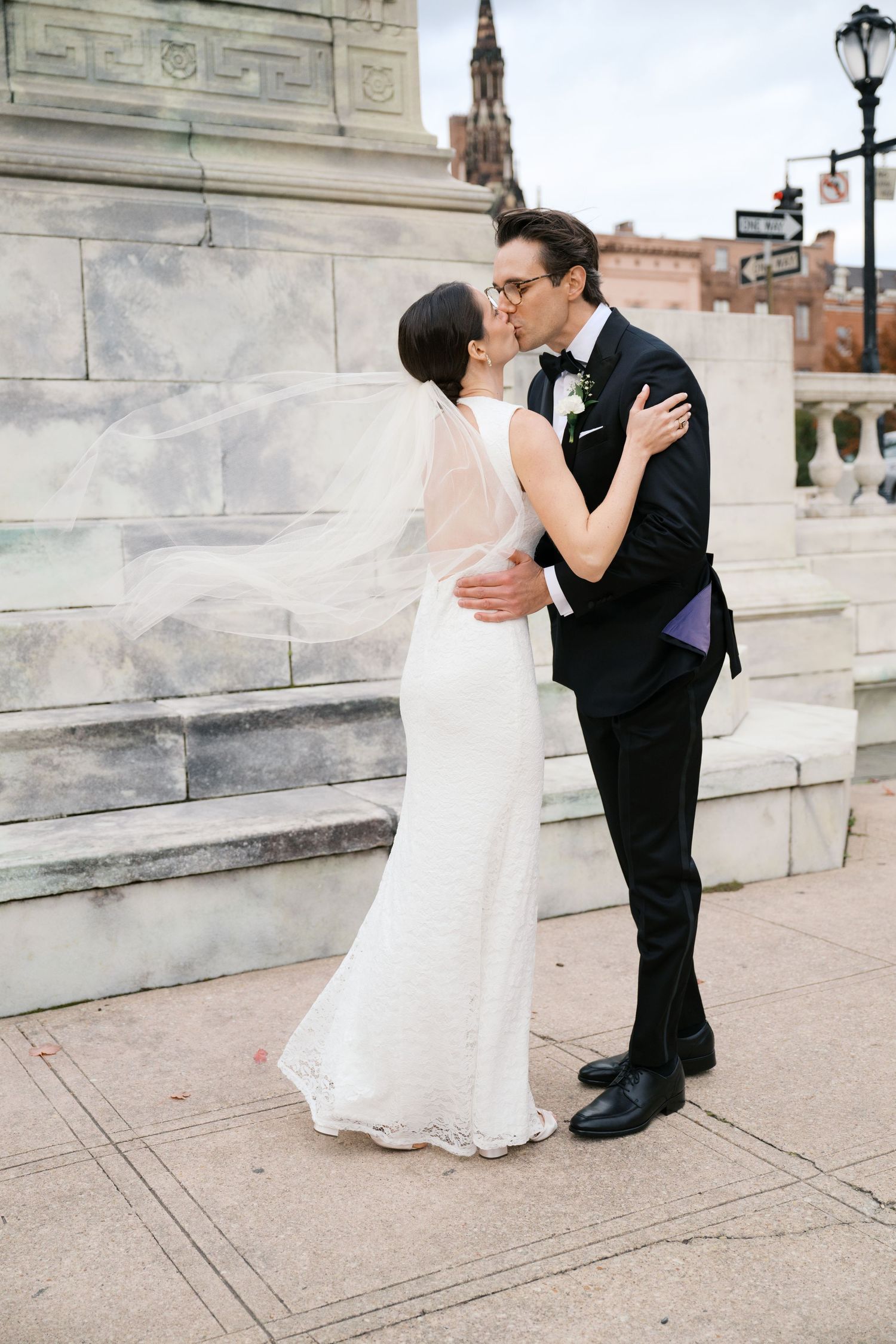 Romantic wedding couple shares intimate moment on marble steps with ornate architecture in background.
