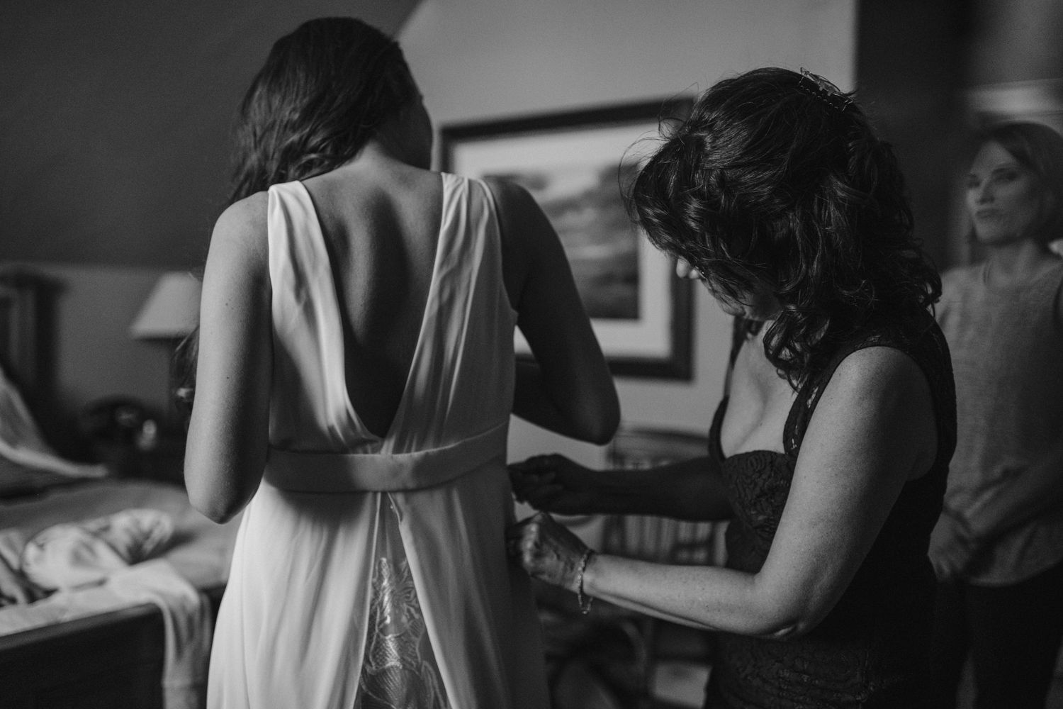 Wedding dress being adjusted and fitted from behind in black and white photograph.