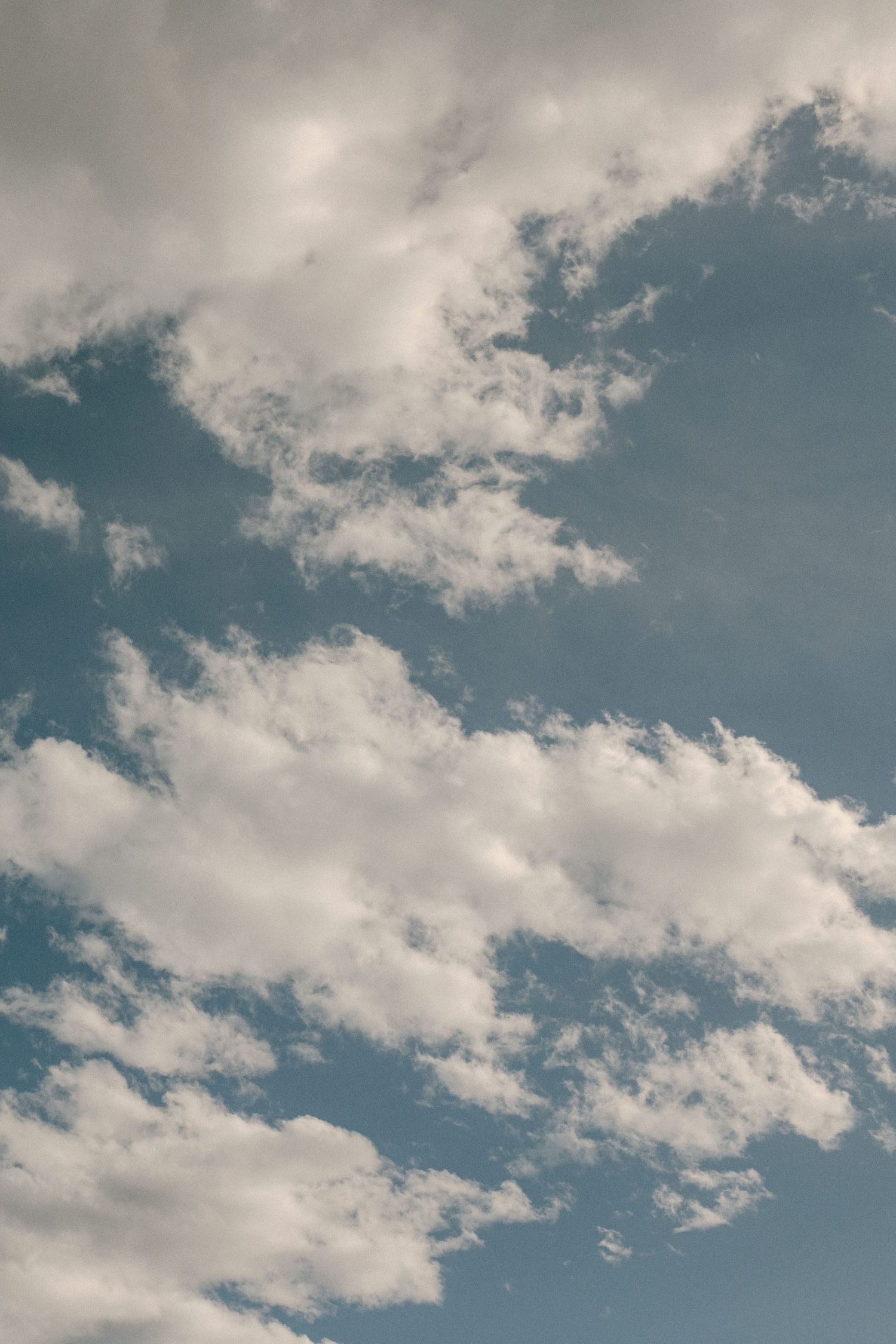 White fluffy clouds float across a bright blue summer sky.