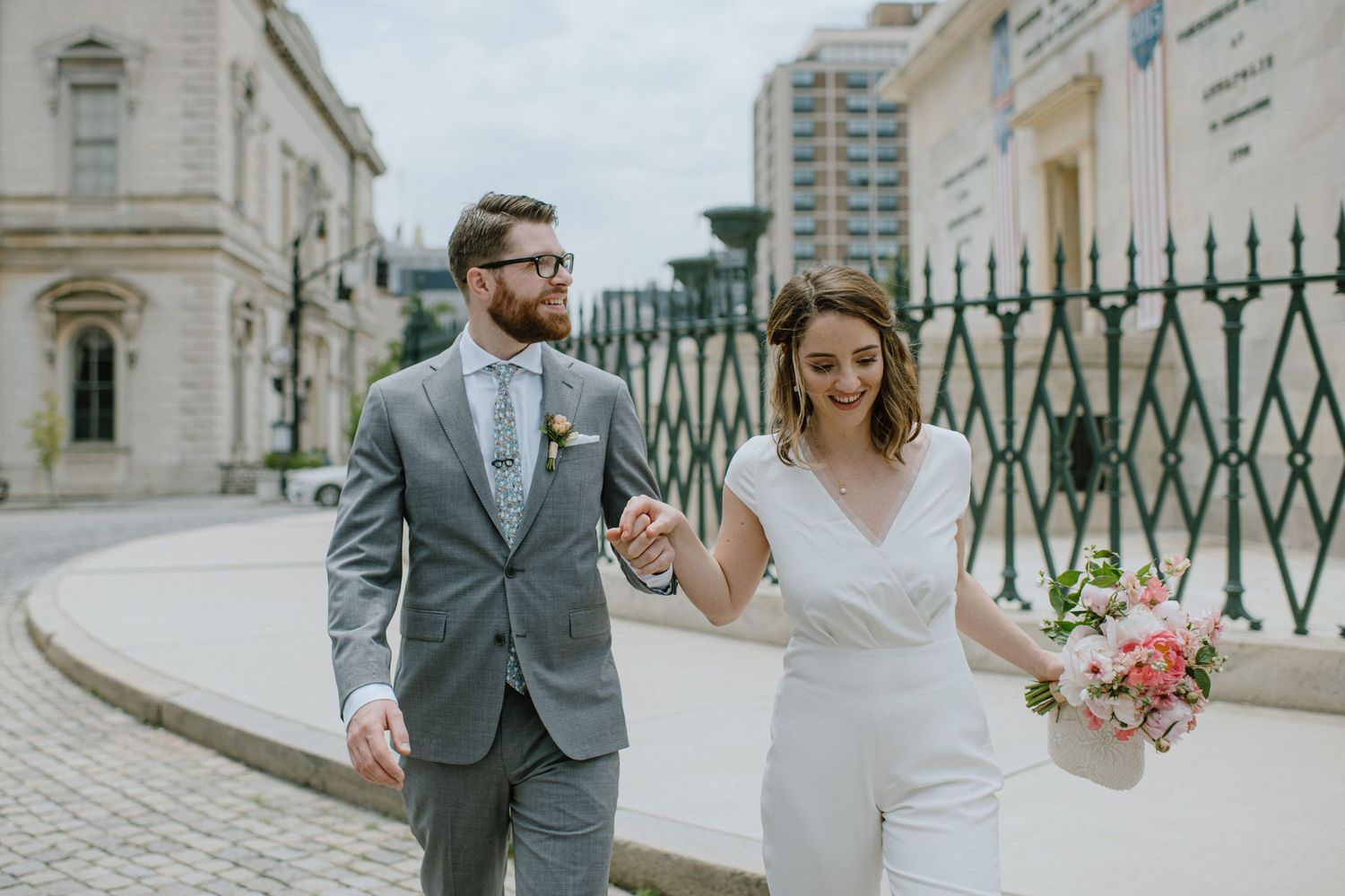 A couple walks along a cobblestone path by ornate iron gates during their wedding day.