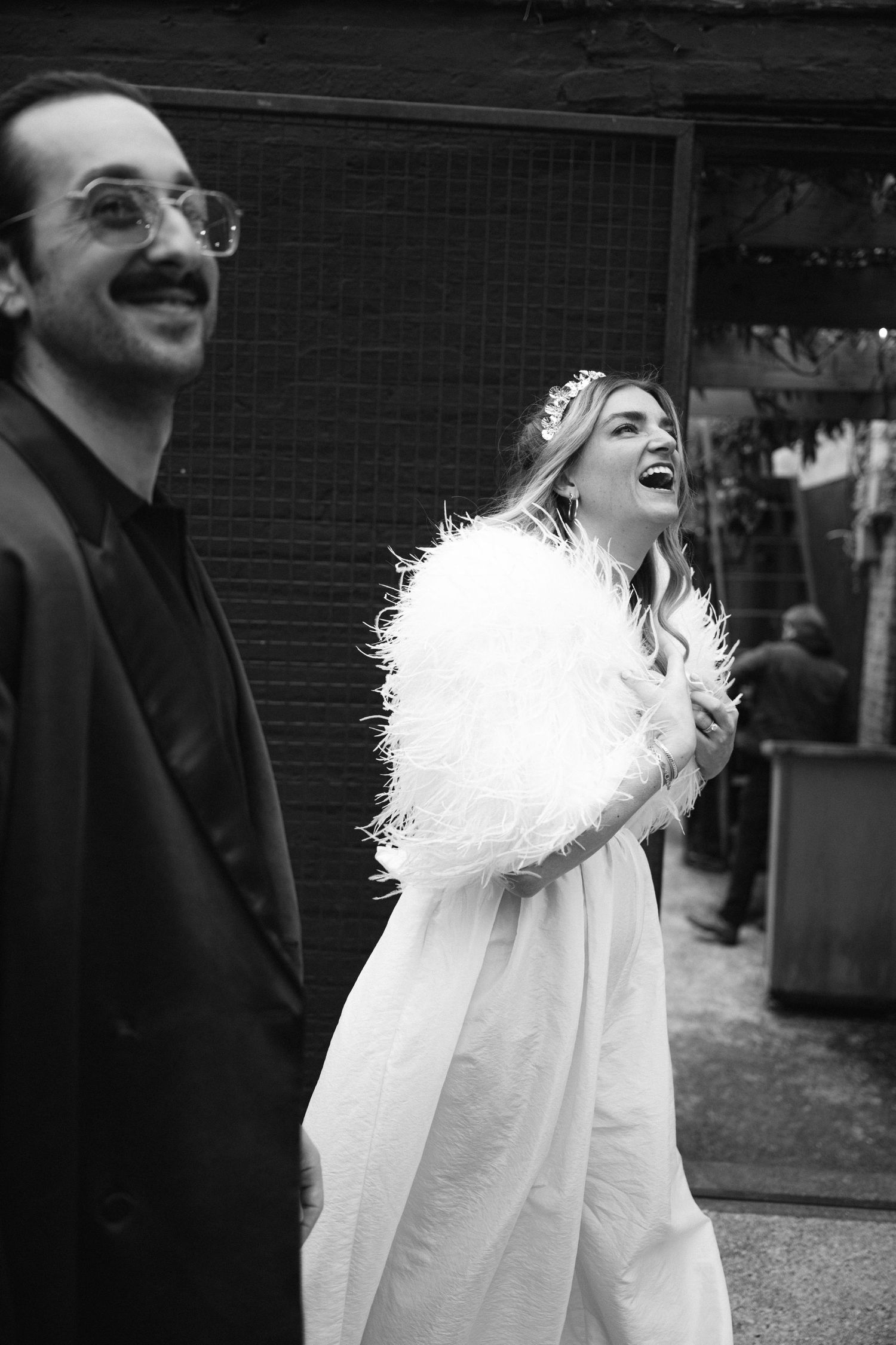 Candid black and white wedding photo showing joyful laughter while wearing white dress and fuzzy shawl at Fadensonnen in Baltimore