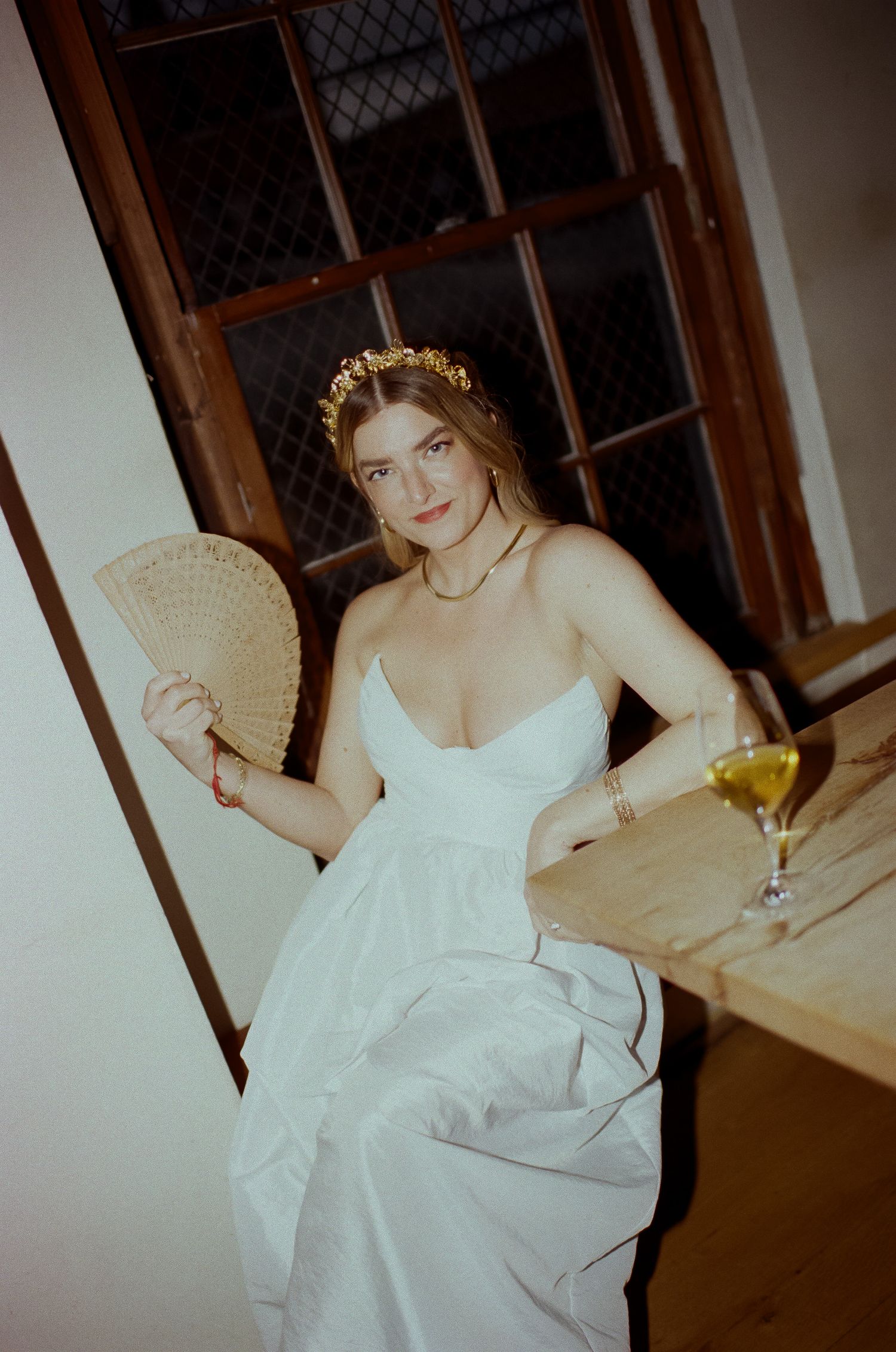 A vintage style photo of someone in a white dress holding a fan and wine glass.