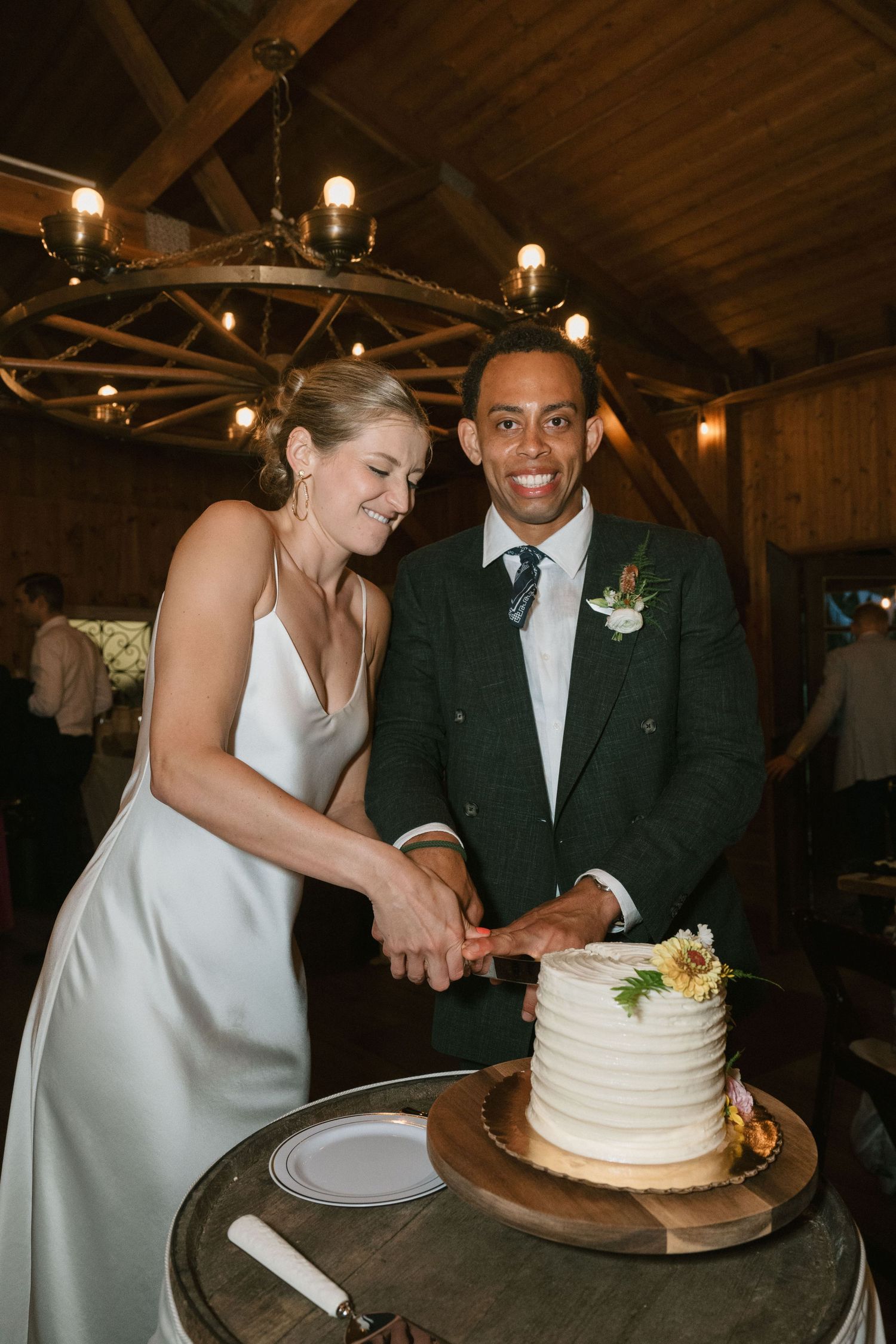 Newlyweds cutting their elegant white wedding cake together in a rustic barn venue.
