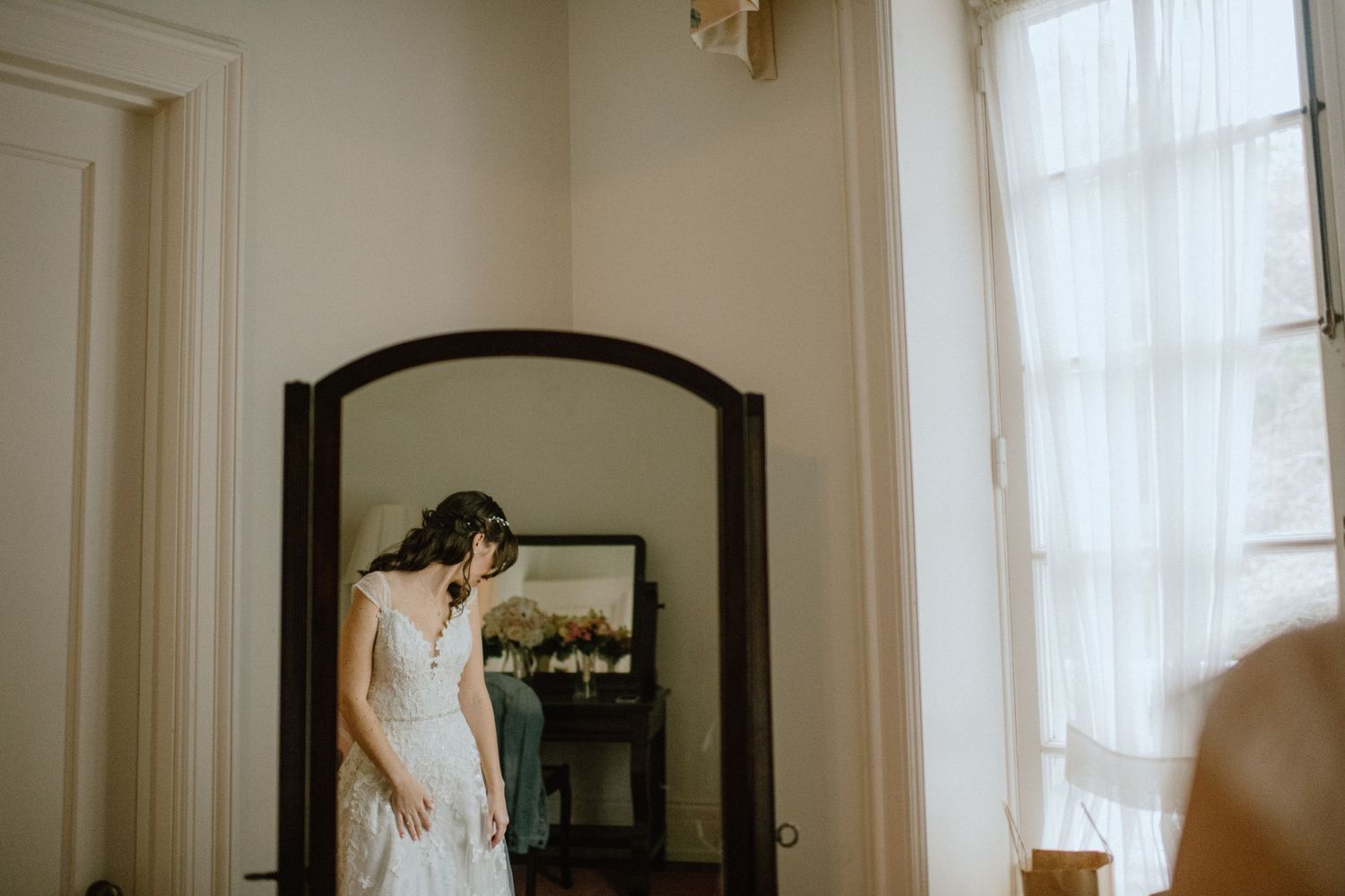 bride getting dressed in wedding dress in mirror