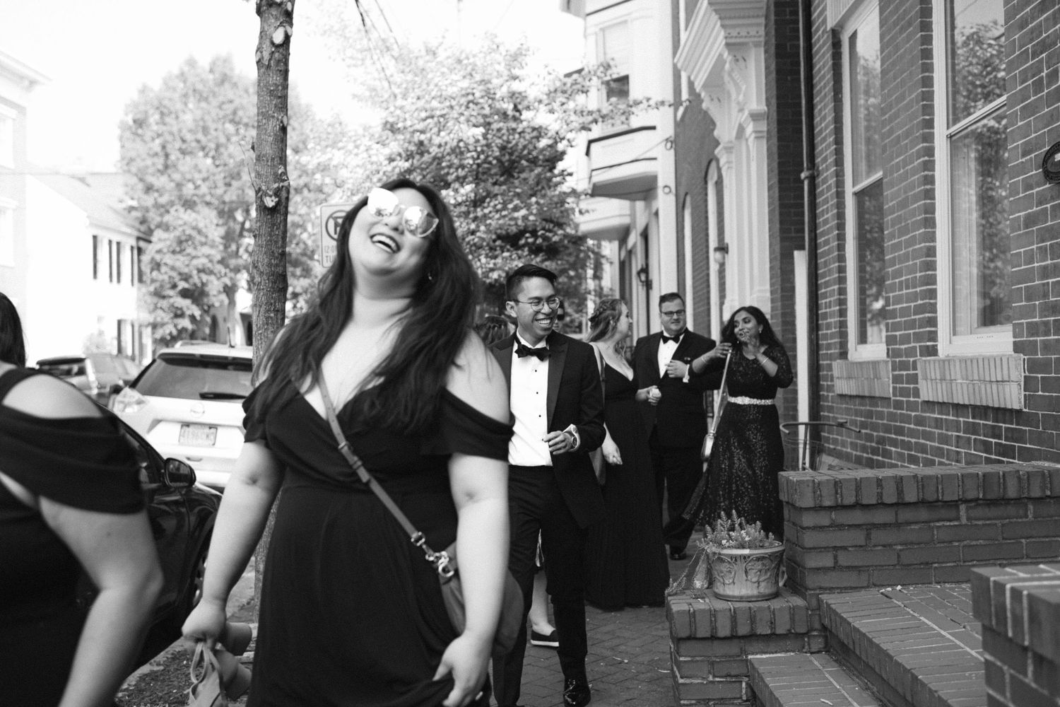 Black and white photo showing people celebrating joyfully on a city street outside a brick building.