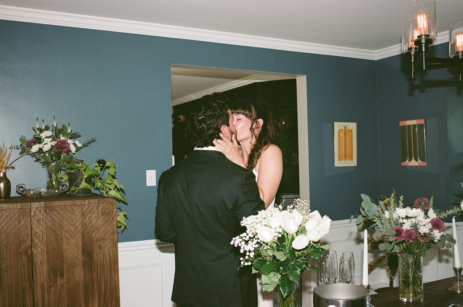 A romantic moment captured in a room with teal walls decorated with floral arrangements and wooden furniture.