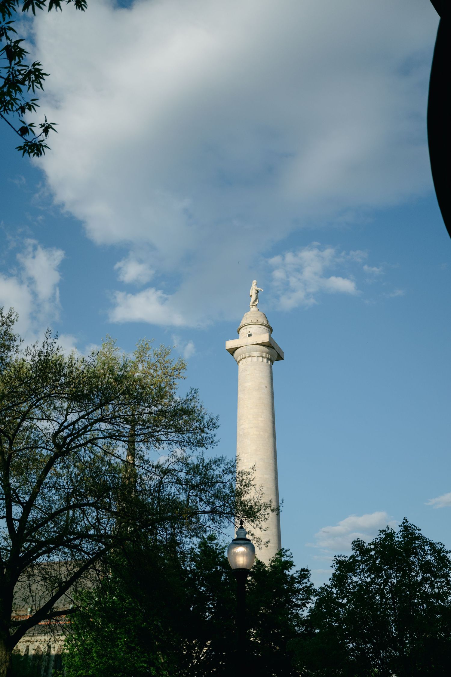 White stone mt. vernon monument tower rises against blue sky with trees framing the view on a sunny day.