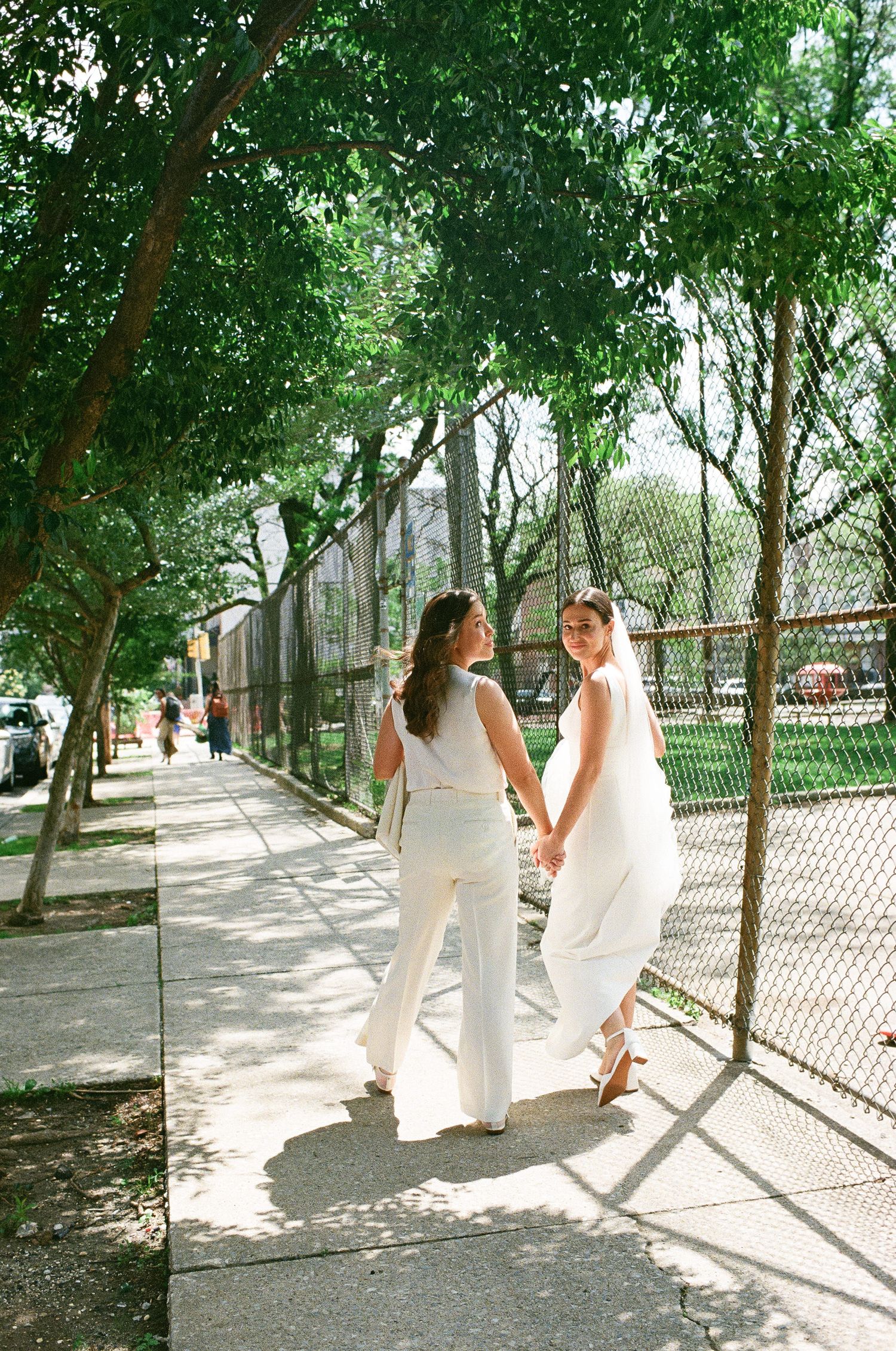 Two people in white outfits sit together on a sunny path surrounded by green trees.