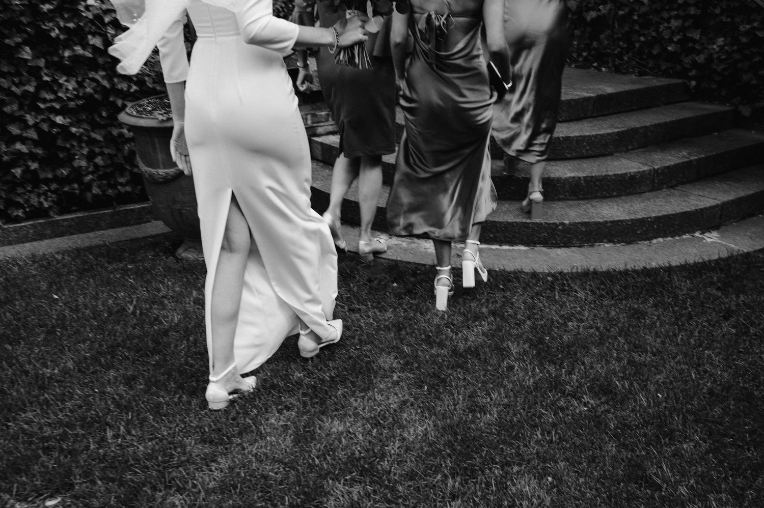 Black and white image of wedding guests walking on grass steps outdoors.