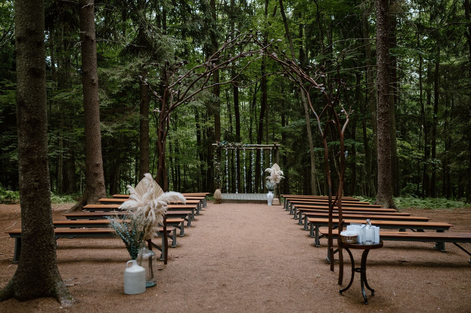 Wooden benches line a forest ceremony site with decorative floral arrangements.