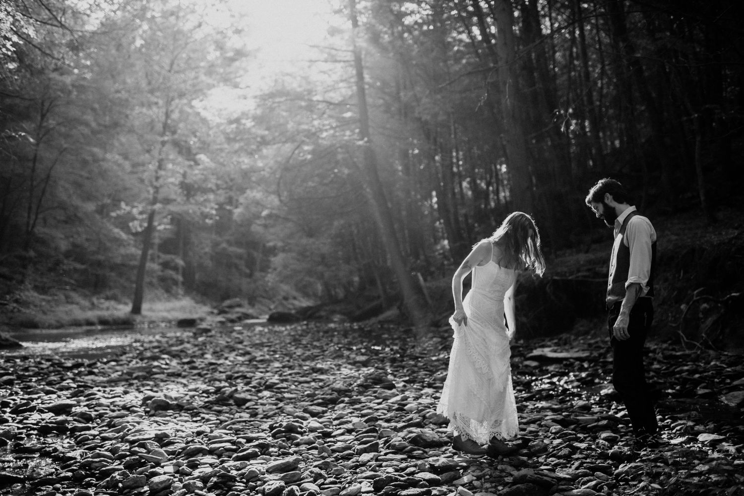 Black and white photo of couple in dreamy forest setting with dramatic lighting.