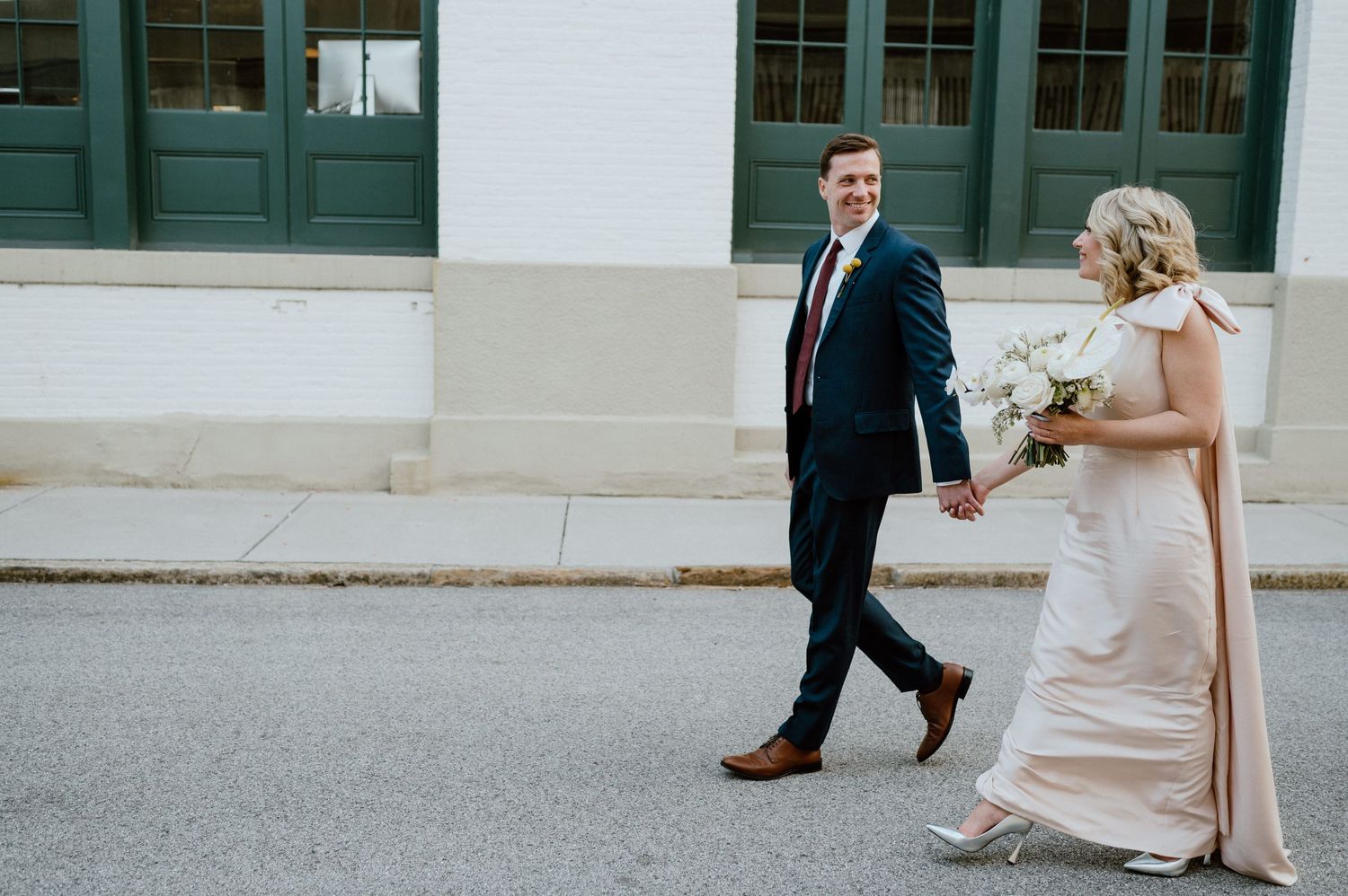 Newlyweds walking together on a city street with green doors in background.
