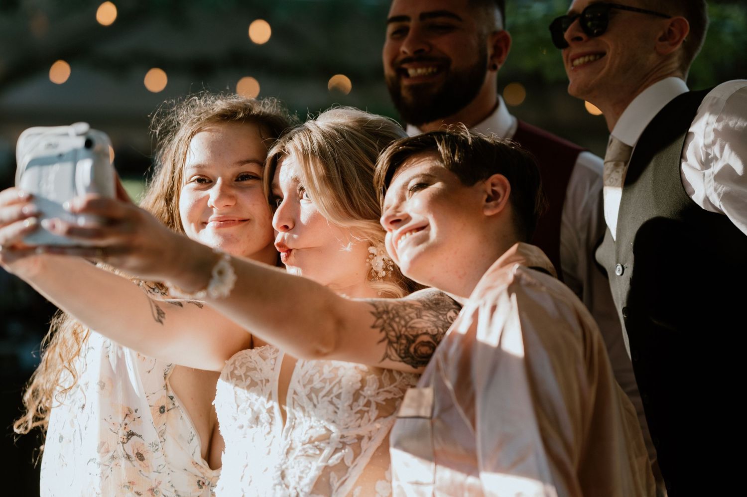 Wedding party takes selfie together during outdoor reception celebration.