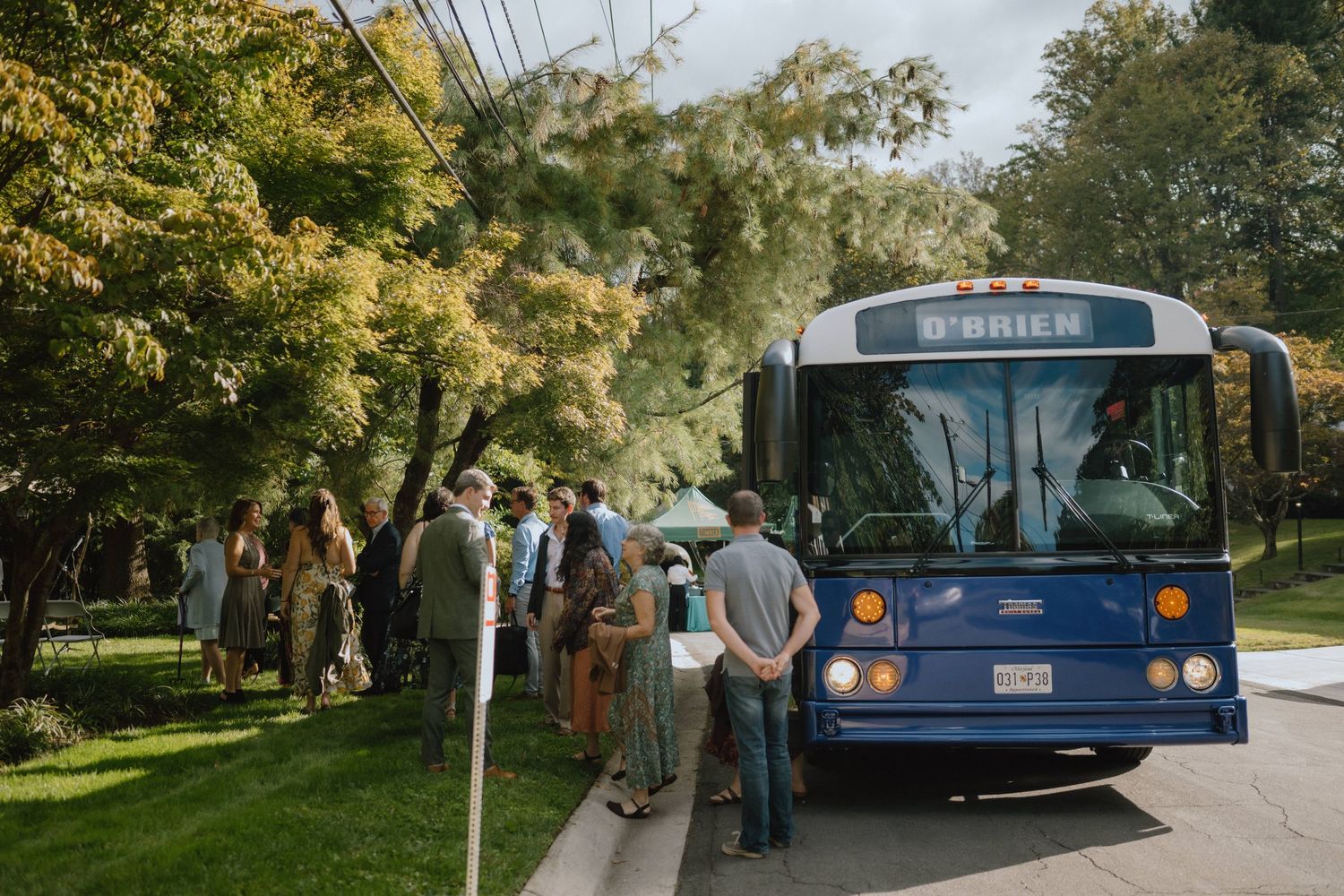 Blue transit bus picking up passengers on tree-lined street.