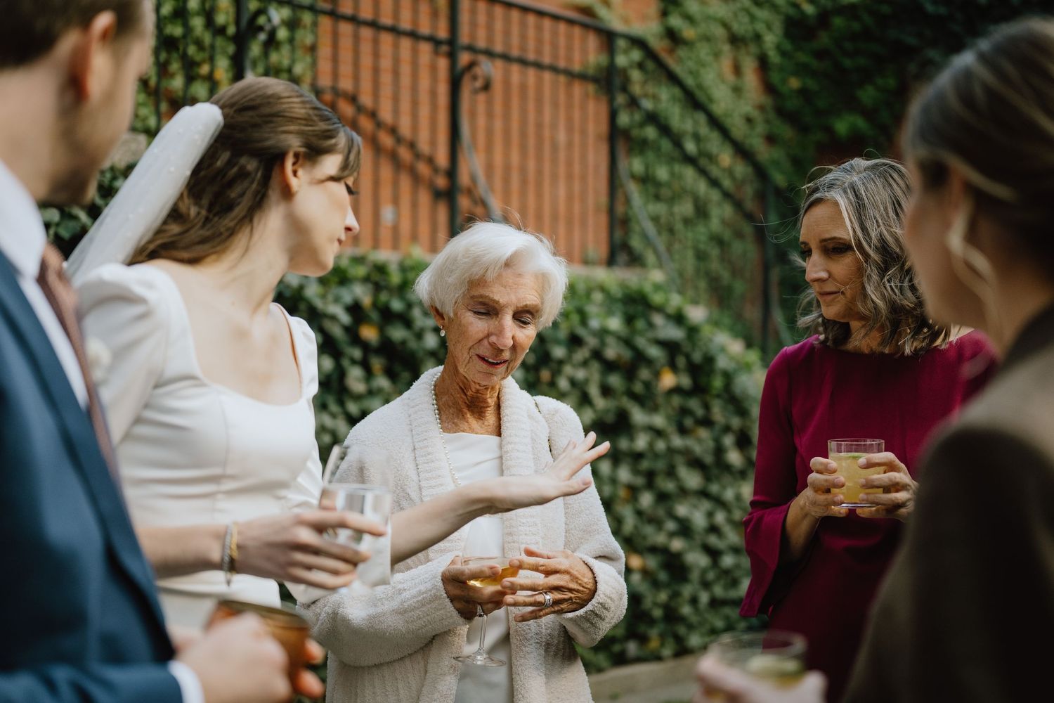 Elegant outdoor wedding reception with guests conversing against an ivy-covered brick wall.