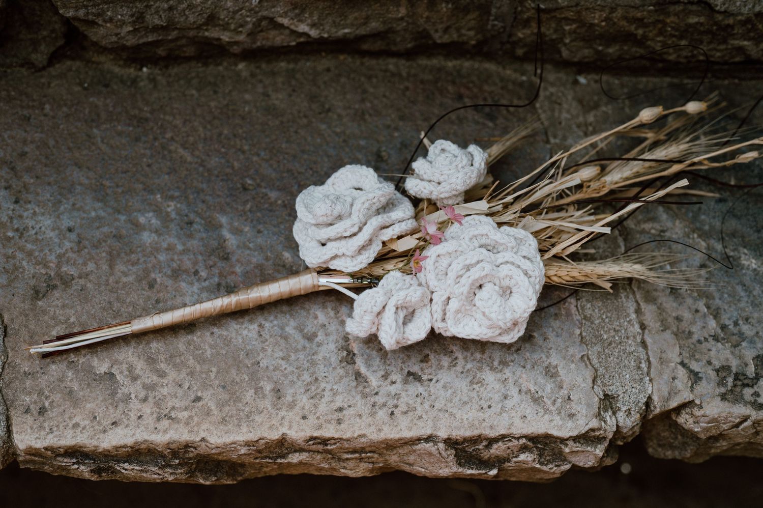 Delicate white fabric flowers with dried stems laid on a stone surface.