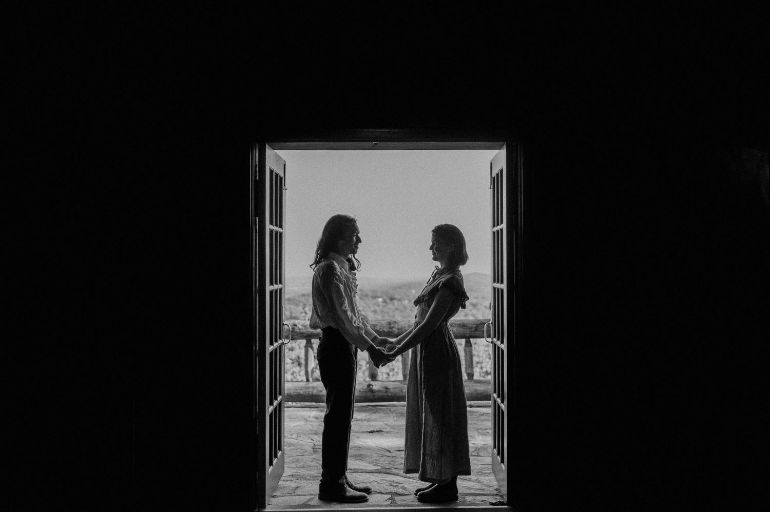 A silhouetted couple standing in a doorway frame against bright light.