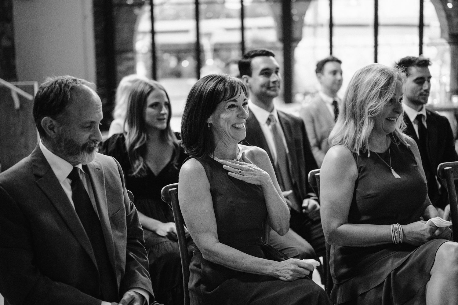 Wedding guests seated in rows watch the ceremony with joyful expressions.