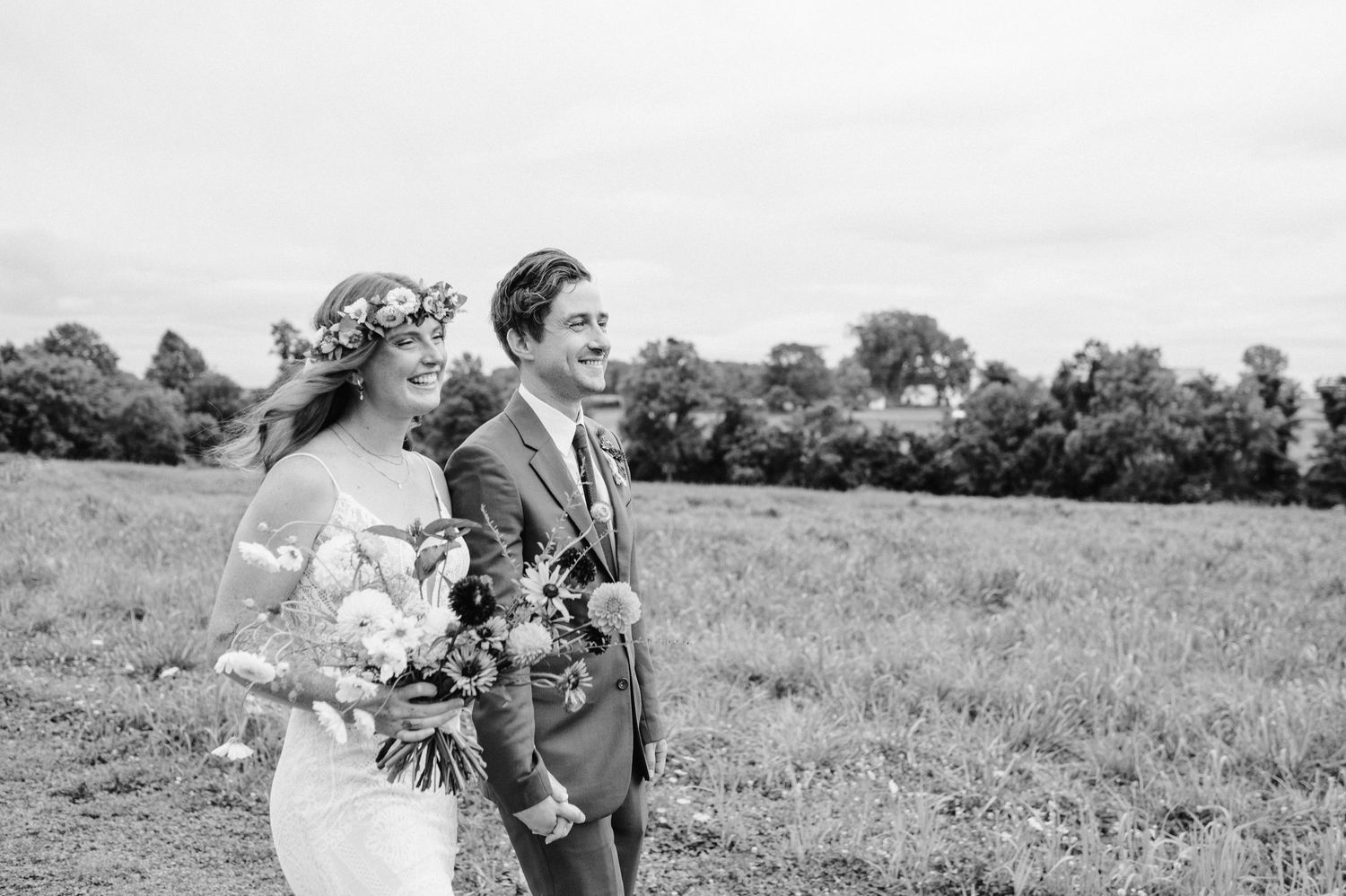 Black and white portrait of wedding couple standing in meadow with florals.