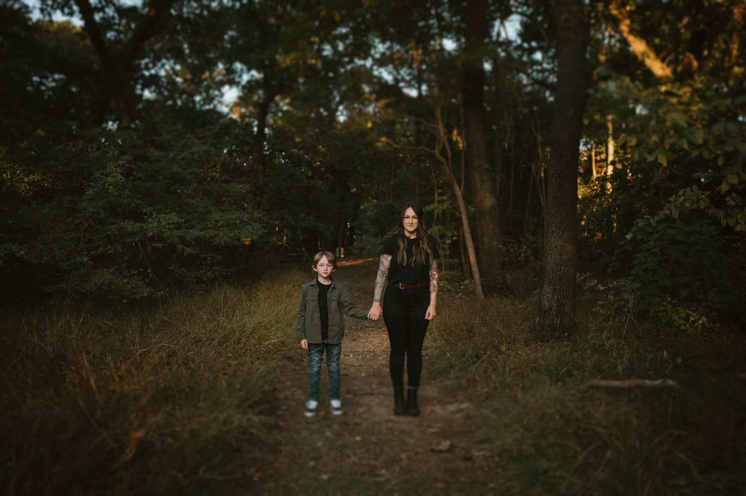 Two people hold hands while walking together on a forest trail at sunset.