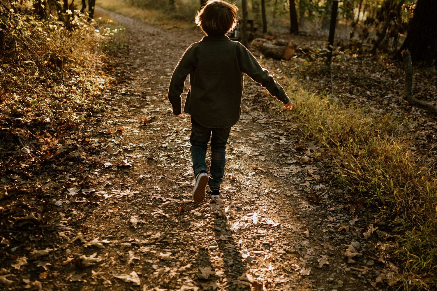A silhouette of a child running along a sunlit forest path creating long shadows.