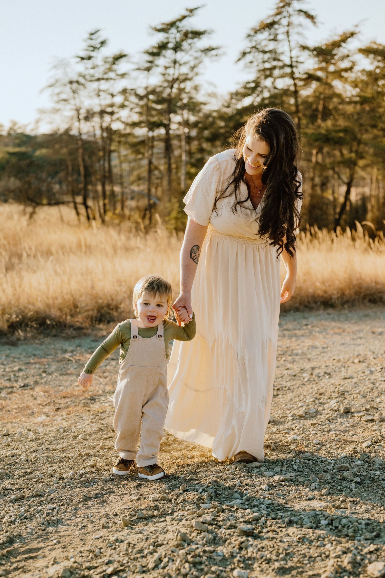 Mother and child walking hand in hand through golden field at sunset.